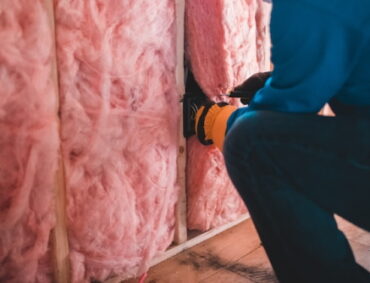 Un trabajador está aplicando aislamiento térmico en una pared con la ayuda de una herramienta. El aislamiento es de un material reflectante y se está instalando cuidadosamente para mejorar la eficiencia energética del edificio.